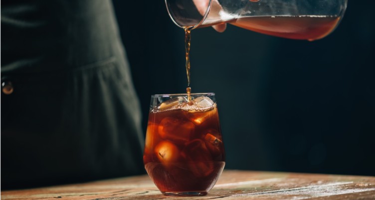 A pitcher of cold brew being poured into a glass with ice