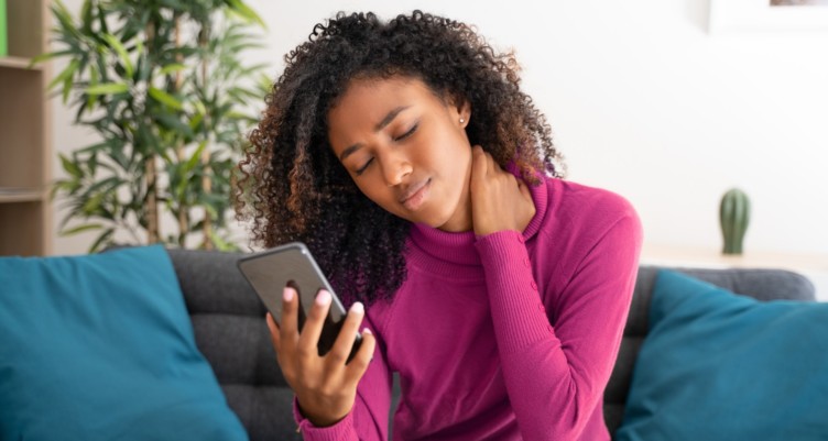 Woman grabbing back of her neck while looking at her cell phone.