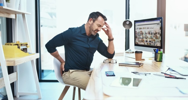 Man grabbing his lower back while sitting in desk chair.
