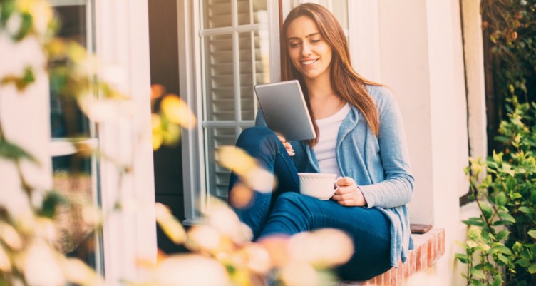 Woman using a tablet while holding a cup of coffee