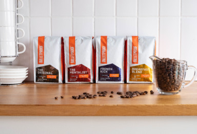 Four bags of Bulletproof Coffee and a measuring cup of coffee beans on a kitchen counter