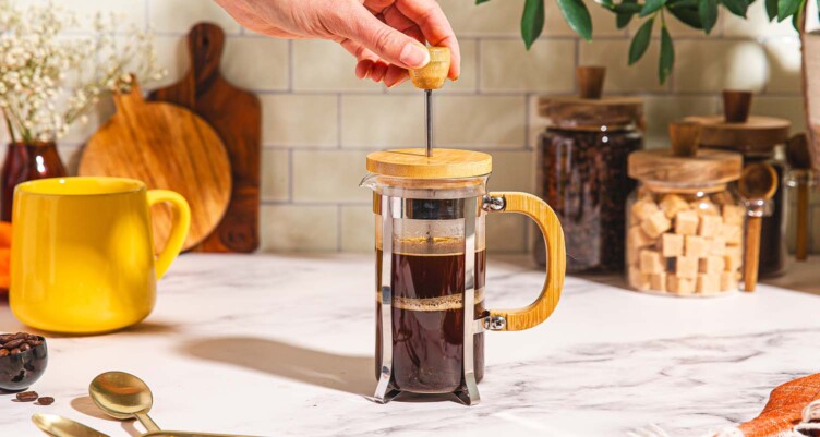Hand pressing down on french press filled with coffee.
