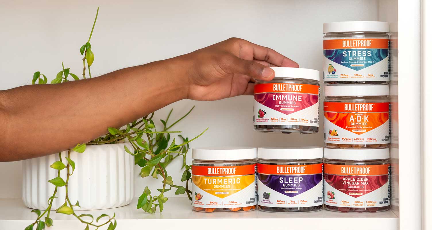 Hand reaching for Bulletproof Sugar-Free Gummy Vitamins collection on a kitchen counter with green plant