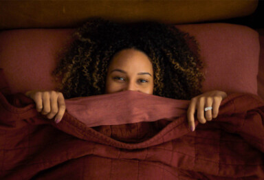 Woman in bed with her eyes peering over the blankets