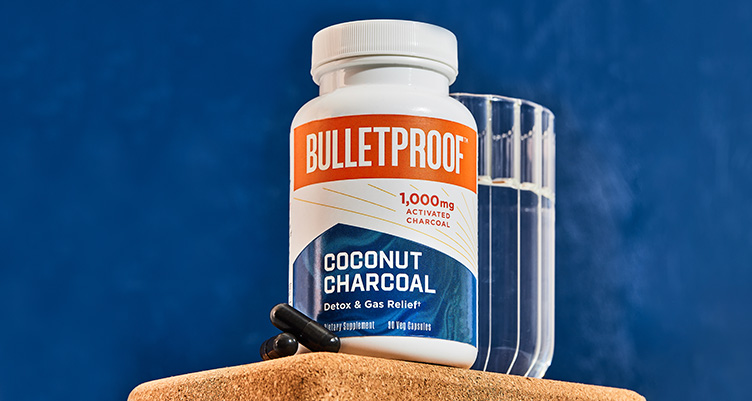 a bottle of bulletproof coconut charcoal pills stands next to a glass of water against a blue background