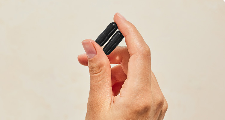 a hand holds 2 coconut charcoal pills against a beige background