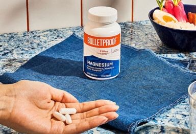 hand holds 3 magnesium pills near a bowl of fruit