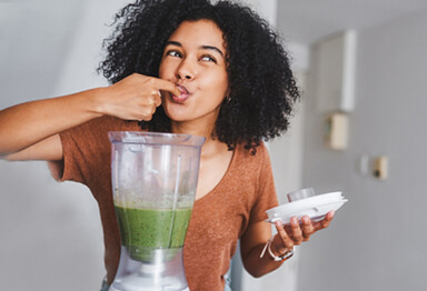 woman licking her finger after dipping it in a blender full of green smoothie