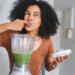 woman licking her finger after dipping it in a blender full of green smoothie