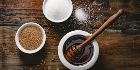 Small pot of honey, brown sugar in a small bowl and white sugar in a small bowl on wood table