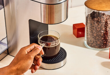fresh coffee under a single serve coffee machine with a jar of coffee beans