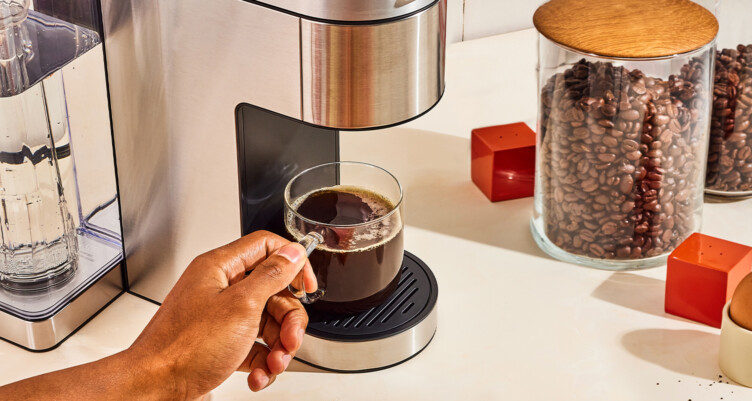 fresh coffee under a single serve coffee machine with a jar of coffee beans