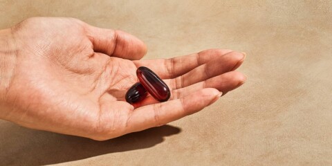 Hand holding 2 gel capsules of fish oil