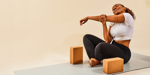 Woman sitting on yoga mat with yoga blocks doing arm stretches and smiling