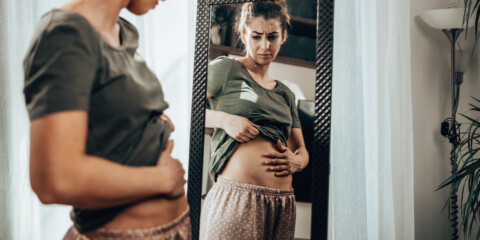 women looking in the mirror holding her stomach as if she is looking at her bloated stomach
