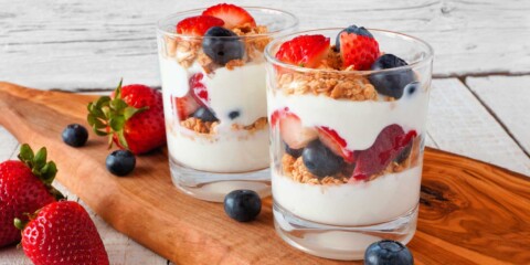 Yogurt parfaits made with berries and granola on wood serving tray