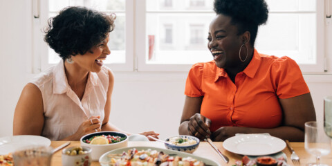 two women laughing while enjoying a meal together