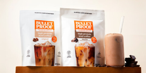 Two bags of Bulletproof High Protein Iced Coffee in Original and Mocha flavor sitting on a pedastal next to a glass of iced coffee with a cream colored background.