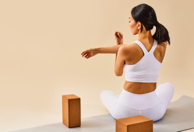 A woman in white workout gear stretching her arm with yoga blocks beside her