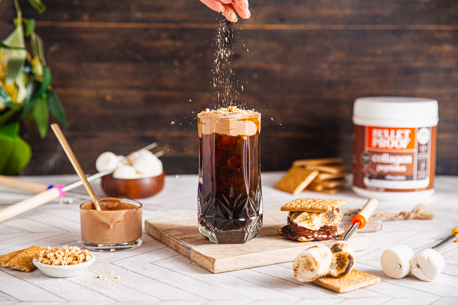 sprinkling topping on coffee next to s'mores