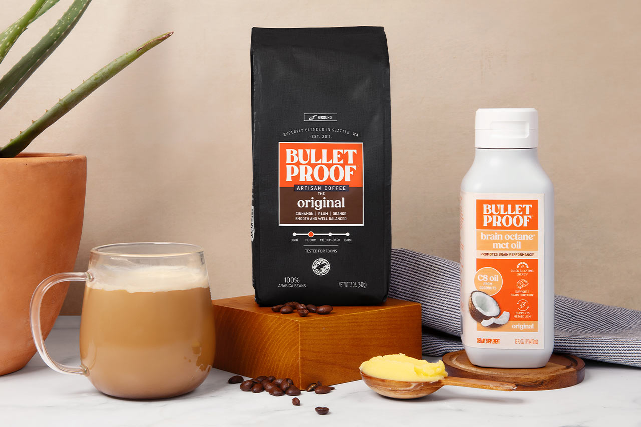 Bulletproof Original Ground Coffee bag, bottle of Brain Octane C8 MCT oil and mug of coffee on kitchen counter with scoop of ghee