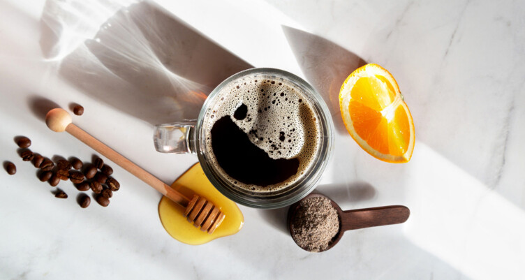 Overhead shot of black coffee, honey stick and orange slices