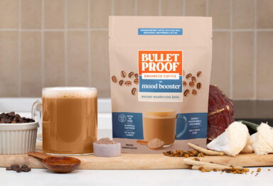 Mood Booster latte packaging next to cup of coffee and functional mushroom pieces